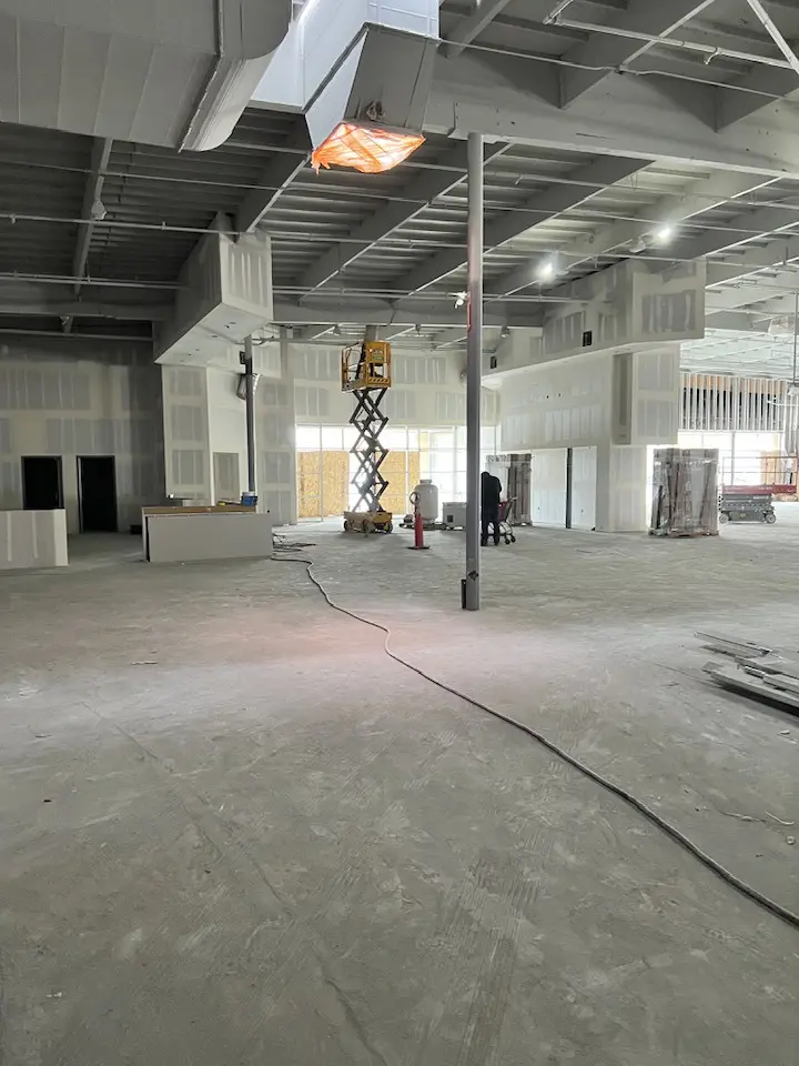 A construction site with a scissor lift in the center and freshly finished drywall.