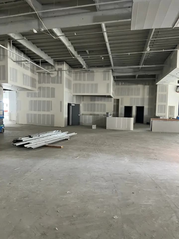 Construction site with a pile of wood in the left corner and freshly finished drywall.